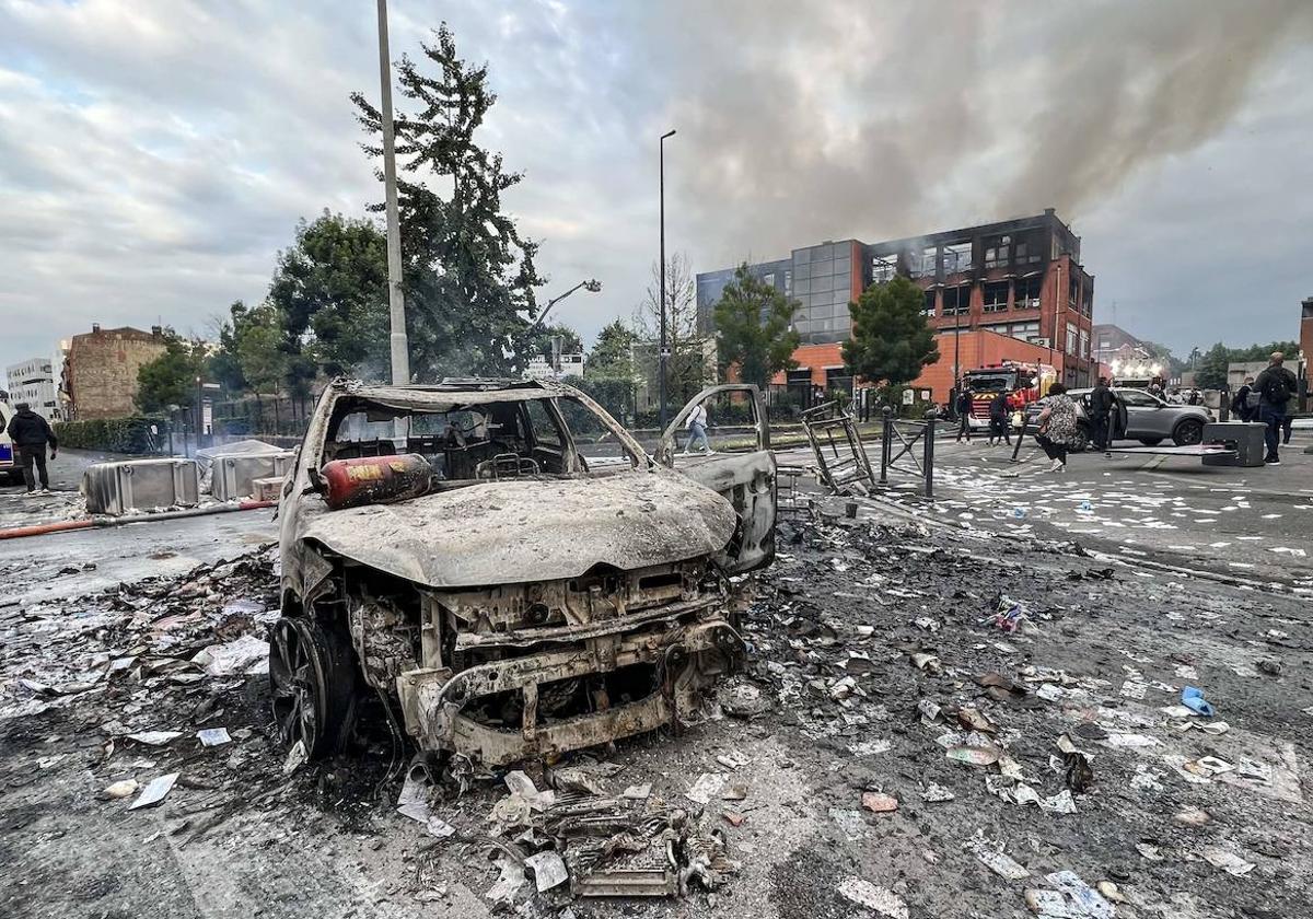 Un grupo de jóvenes transita junto a un coche calcinado en la localidad de Roubaix.