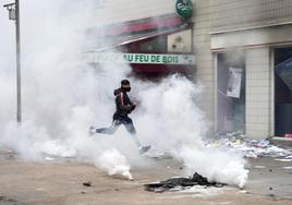 Un joven avanza entre una nube de gas lacrimógeno para lanzar una pieza pirotécnica a las fuerzas de seguridad.