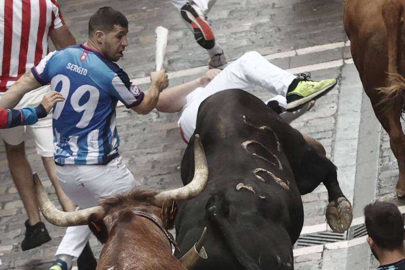 Un mozo cae ante uno de los toros de la ganadería de Núñez del Cuvillo a su paso por la calle de la Estafeta.