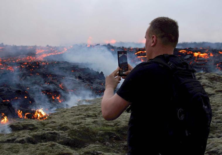 Un hombre toma una fotografía de la erupción de un volcán cerca de Reykjanes, capital de Islandia