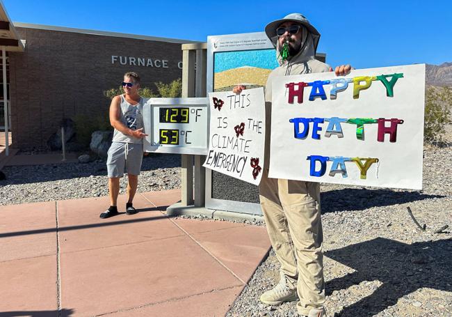 Un hombre sostiene pancartas frente a un letrero digital que muestra la temperatura más alta registrada en el Valle de la Muerte, en California