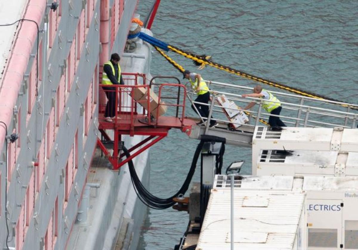 Operarios transportan varias cajas al interior del buque 'Bibby Stockholm', donde vivirán centenares de migrantes.