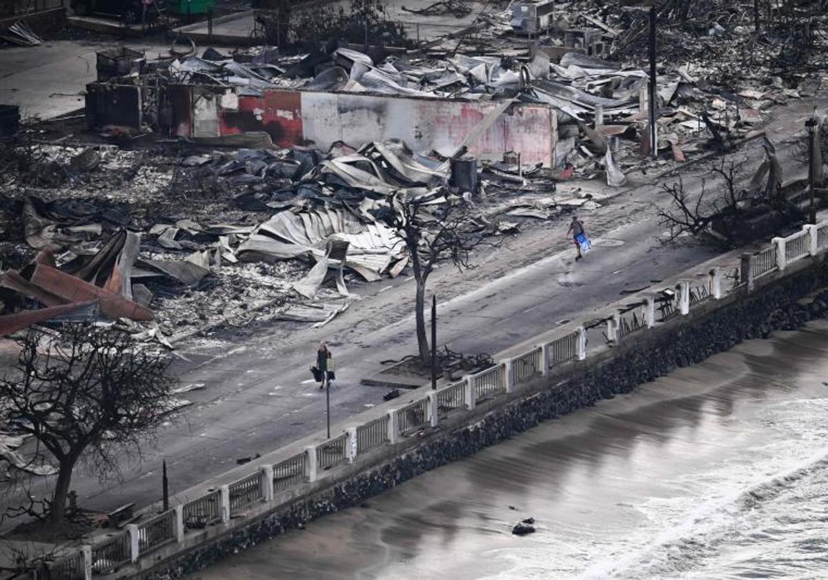 Residentes cargados con sus pertenencias caminan junto a los edificios devastados por los incendios en la isla hawaiana de Maui.