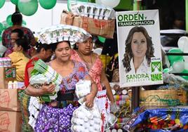 Una mujer camina por un mercado guatemalteco junto a un cartel de la candidata Sandra Torres.