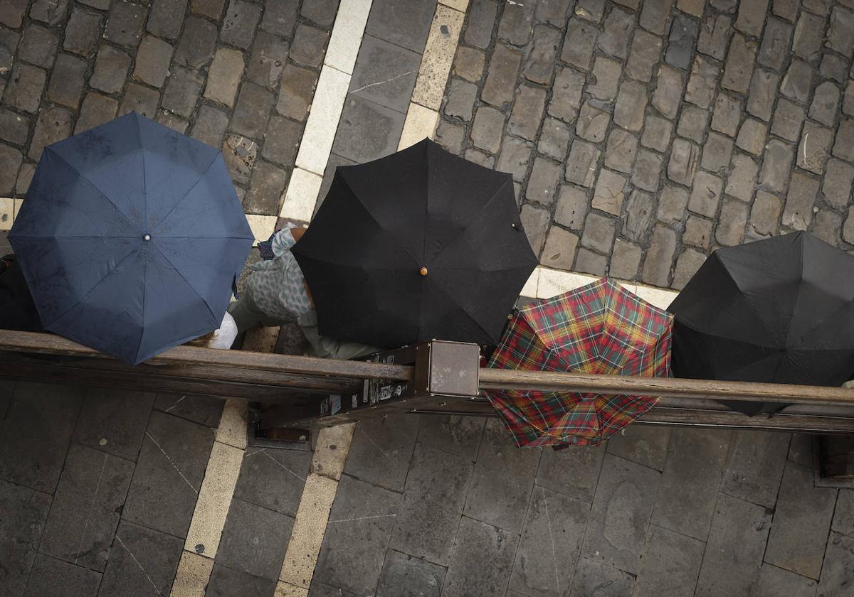 Varias personas se protegen de la lluvia en Pamplona.