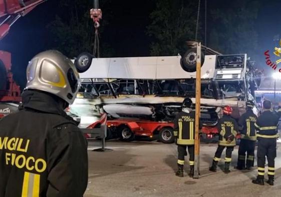 Bomberos retiran los restos del autobús que cayó de un puente y se incendió en la localidad italiana de Mestre.