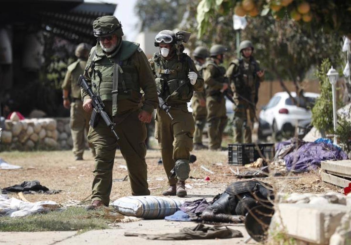 Soldados israelíes caminan junto al cuerpo del militante de Hamás abatido en el kibutz de Kfar Aza, junto a la frontera con Gaza.