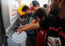 Varios ciudadanos hacen cola para llenar botellas y garrafas con agua.