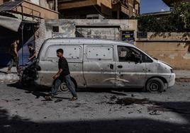 Viandantes caminan junto a un vehículo destruido en la ciudad siria de Idlib.