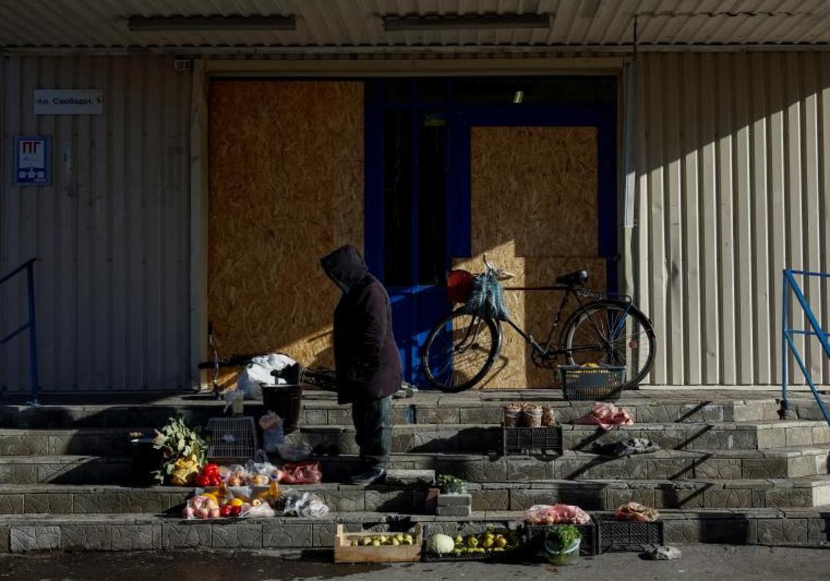 Una mujer vende verduras en las escaleras de un supermercado cerrado, en la región de Donetsk.