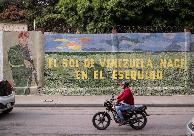 Un hombre conduce una moto frente a un mural que dice «El sol de Venezuela nace por El Esequibo»