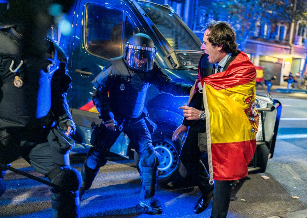 Imagen secundaria 1 - En la imagen superior, radicales y encapuchados se hicieron una noche más con la cabecera de la concentración de protesta a última hora; debajo, dos policias antidisturbios agarran a una persona envuelta con la bandera española y, por último, uno de los contenedores que fueron quemados por los violentos cerca de la madrileña calle Ferraz durante los altercados.