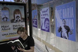 Una joven lee junto a varios carteles electorales en Argentina.