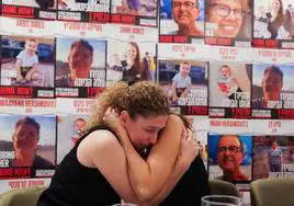 Dos mujeres cuyos familiares fueron secuestrados se consuelan mutuamente durante una rueda de prensa en Tel Aviv ante carteles de los rehenes.
