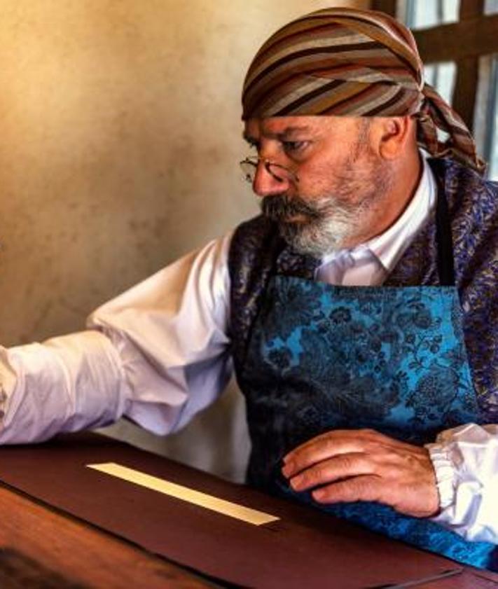 Imagen secundaria 2 - Tony Arellano pertenece a la quinta generación de una familia de artesanos espaderos toledanos. En Puy du Fou es Antonio de Vivar. A la drecha, una artesana del obrador Santo Tomé, de Toledo, elabora mazapán tradicional en su puesto de Puy du Fou. A la izquierda, Maese Alfonso es el amanuense iluminador del parque, que tiene un taller de caligrafía e ilustración.