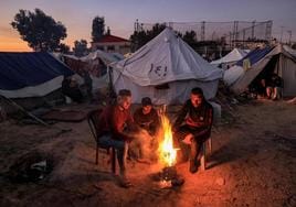 Los palestinos se calientan alrededor de un fuego fuera de una de las tiendas que albergan a los desplazados por el conflicto en Gaza.