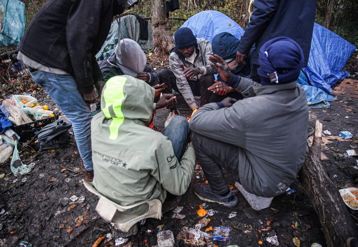 Migrantes sudaneses se sientan junto al fuego cerca de sus tiendas de campaña en Calais, en Francia