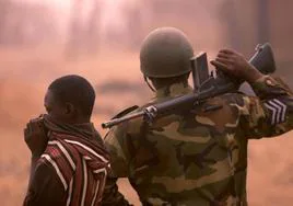 Un jóven nigeriano se tapa la nariz como consecuencia del olor a muerte de un poblado nigeriano mientras un soldado examina la zona.