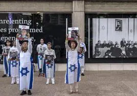 Varias personas envueltas en banderas israelíes sostienen retratos de algunos de los rehene.