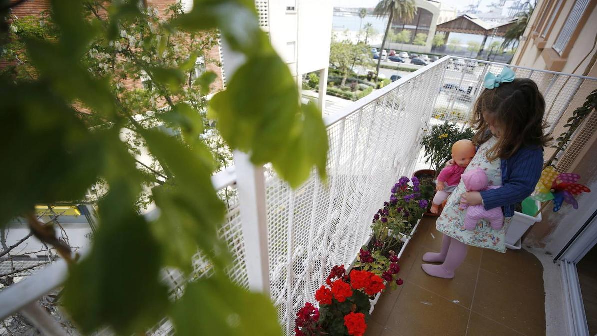 Una niña juega con sus muñecas en el balcón de casa.