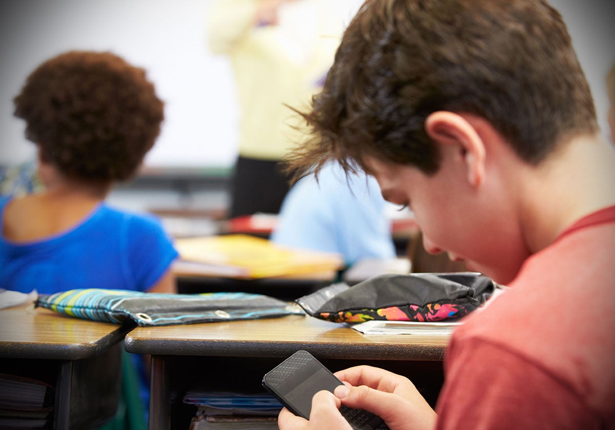 Un niño mira el móvil en clase.