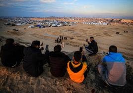 Palestinos desplazados que utilizan tarjetas eSIM intentan obtener una señal para ponerse en contacto con sus familiares en una colina frente a su campamento improvisado en Rafah.