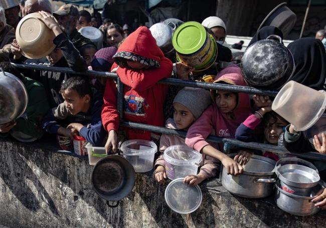 Palestinos desplazados sostienen ollas y cubos vacíos mientras esperan a recibir alimentos en el campo de refugiados de Rafah.