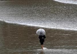 Una mujer con paraguas pasea por una playa de Asturias en una imagen tomada el pasado octubre. Está previsto que las lluvias vuelvan al Principado a partir de este jueves.