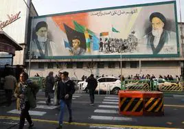 Viandantes caminan por una calle de Teherán en la que se exhibe en un mural el rostro del ayatolá Alí Jamenéi y su predecesor.