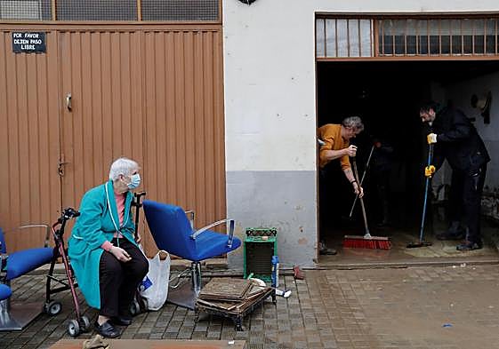 Una mujer observa a dos voluntarios achicando agua de su casa tras las inundaciones registradas en Villava, Navarra.