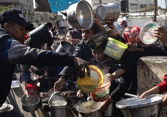 Palestinos con cazuelas para recibir alimentos en el campo de refugiados de Rafah