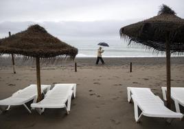 Una persona camina por la playa de Los Álamos en Torremolinos, bajo la lluvia.