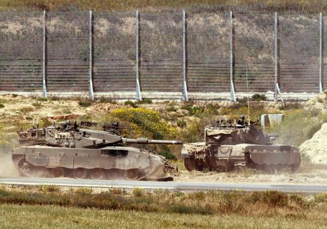 Dos tanques israelíes avanzan hacia una valla fronteriza.