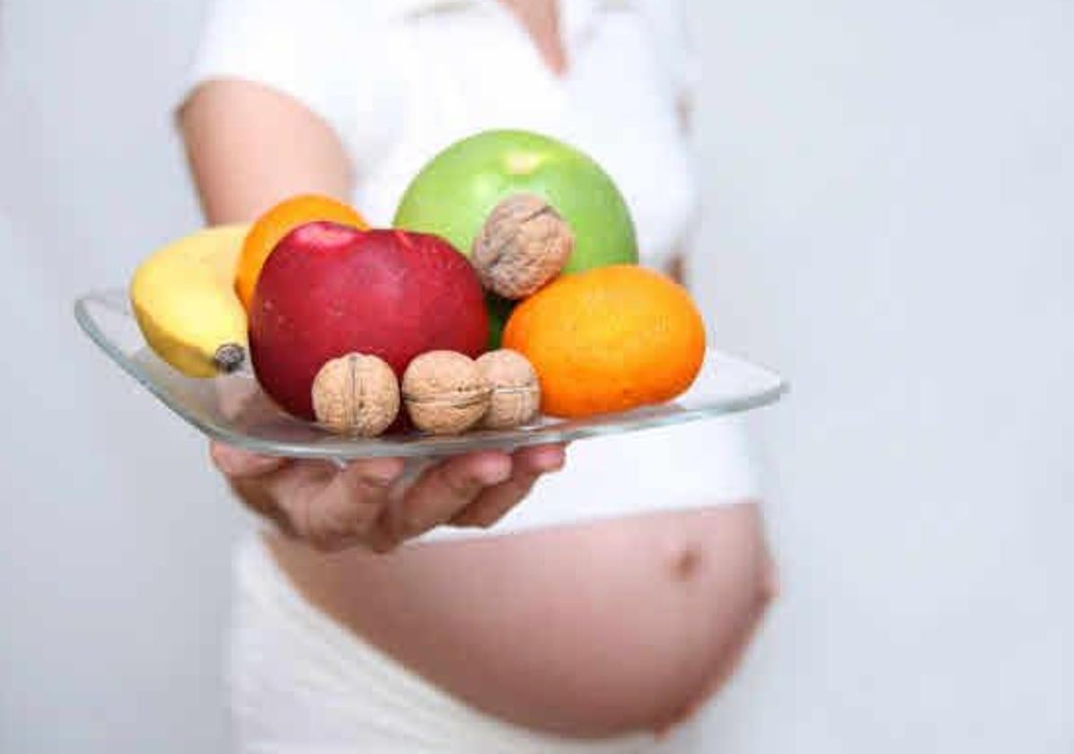 Mujer embarazada muestra un plato con frutas.