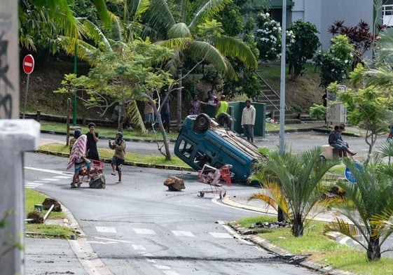 Un grupo de manifestantes se congrega cerca de un automóvil volcado en la capital de Nueva Caledonia, Noumea.