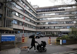 Una mujer camina con su perro y su bebé frente a la entrada del centro NHS Tavistock.