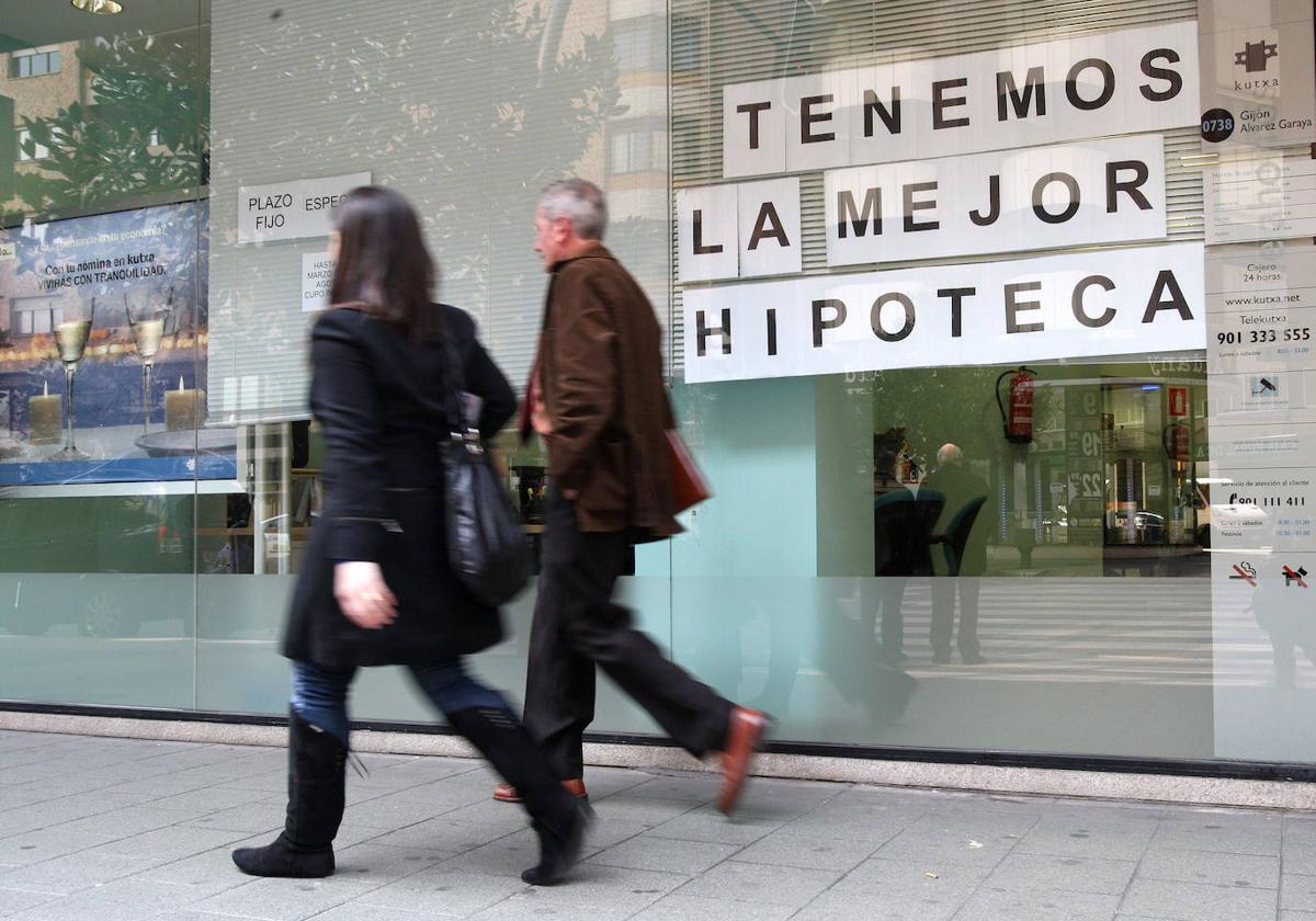 Viandantes ante el escaparate de un banco con una oferta hipotecaria.