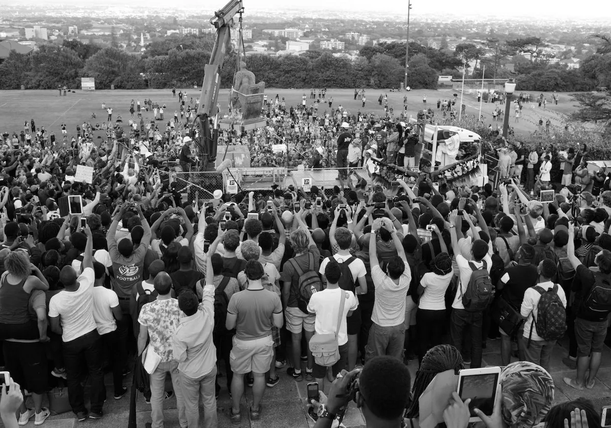 Imagen principal - 'El derrocamiento de Cecil John Rhodes después de arrojar heces humanas contra la estatua y de que la universidad accediera a las demandas de los estudiantes para su retirada, Universidad de Ciudad del Cabo, 9 de abril de 2015' / 'En la oficina de la funeraria, Orlando West, Soweto', 1972 / 'El hijo de un criador de avestruces espera junto a un jornalero a que comience la jornada de trabajo, cerca de Oudtshoorn, Provincia del Cabo Occidental, 1966.