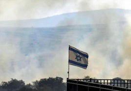 Una bandera israelí ondea entre columnas de humo causadas por los cohetes lanzados por Hezbolá.