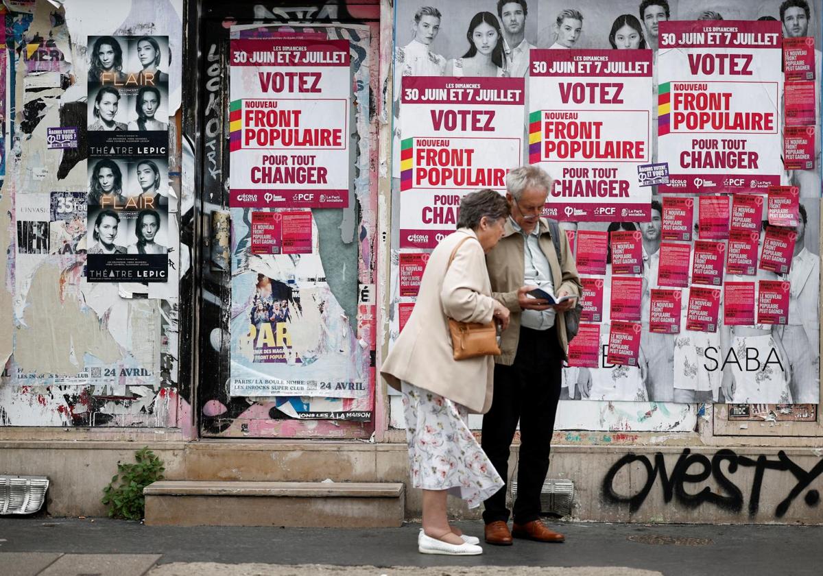 Una pareja de turistas consulta una guía de París frente a un panel electoral con carteles del Frente Popular.