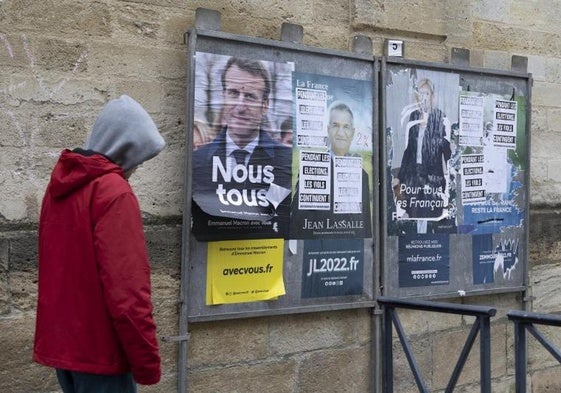 Un hombre camina frente a un mural con carteles electorales.