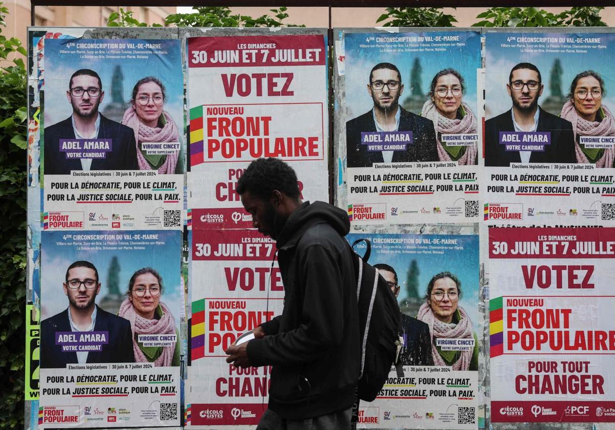 Un hombre pasa junto a carteles electorales de la alianza izquierdista Nuevo Frente Popular.