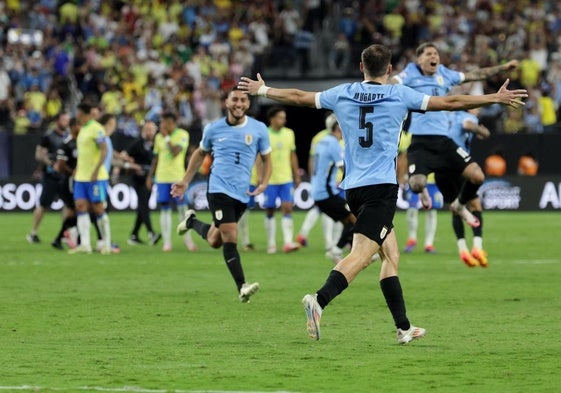 Los futbolistas uruguayos celebran la victoria en los penaltis con los brasileños de fondo.