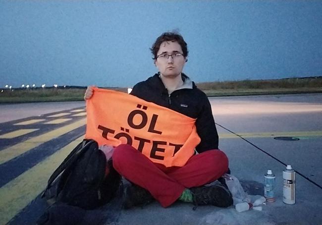 Uno de los activistas que accedió al aeropuerto Hamburgo, con su mano pegada en una de las pistas y en la otra un cartel contra el uso del petróleo.