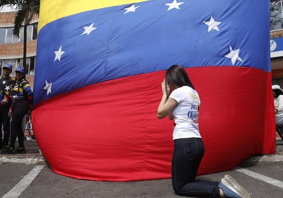 Una mujer reza delante de una bandera venezolana.