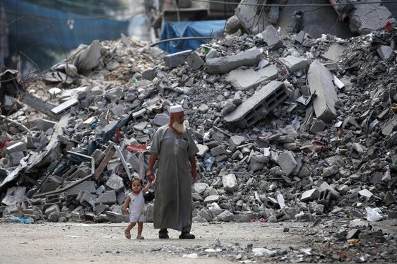 Un hombre camina con su nieta entre las ruinas de Gaza City.