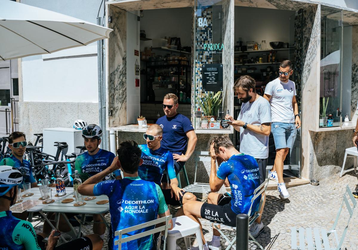 Los ciclistas del Decathlon, relajados tomando algo en una terraza con Ben O'Connor en primer plano, de espaldas.