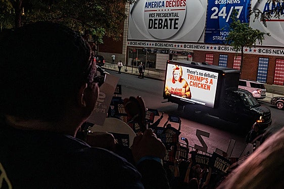 Ambiente en el exterior de los estudios de la CBS en Nueva York, con periodistas, curiosos y una crítica incluida a Trump en un camión.