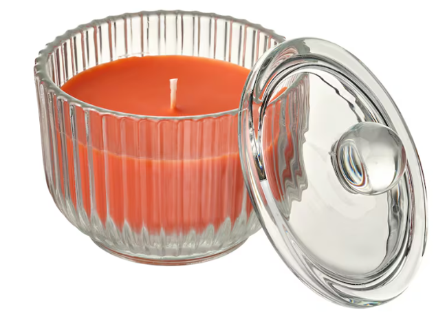 Vela decorativa naranja en recipiente transparente con tapa.