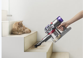 Aspiradora de mano Dyson v8 succionando el  pelo enfrente de un gato naranja.